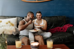 two men sitting on a couch eating pizza