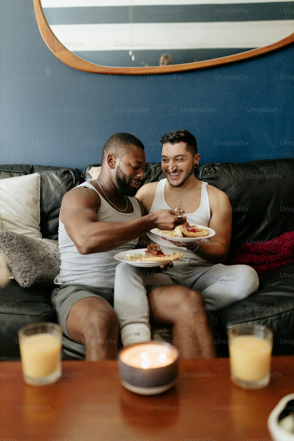 a couple of men sitting on a couch eating food