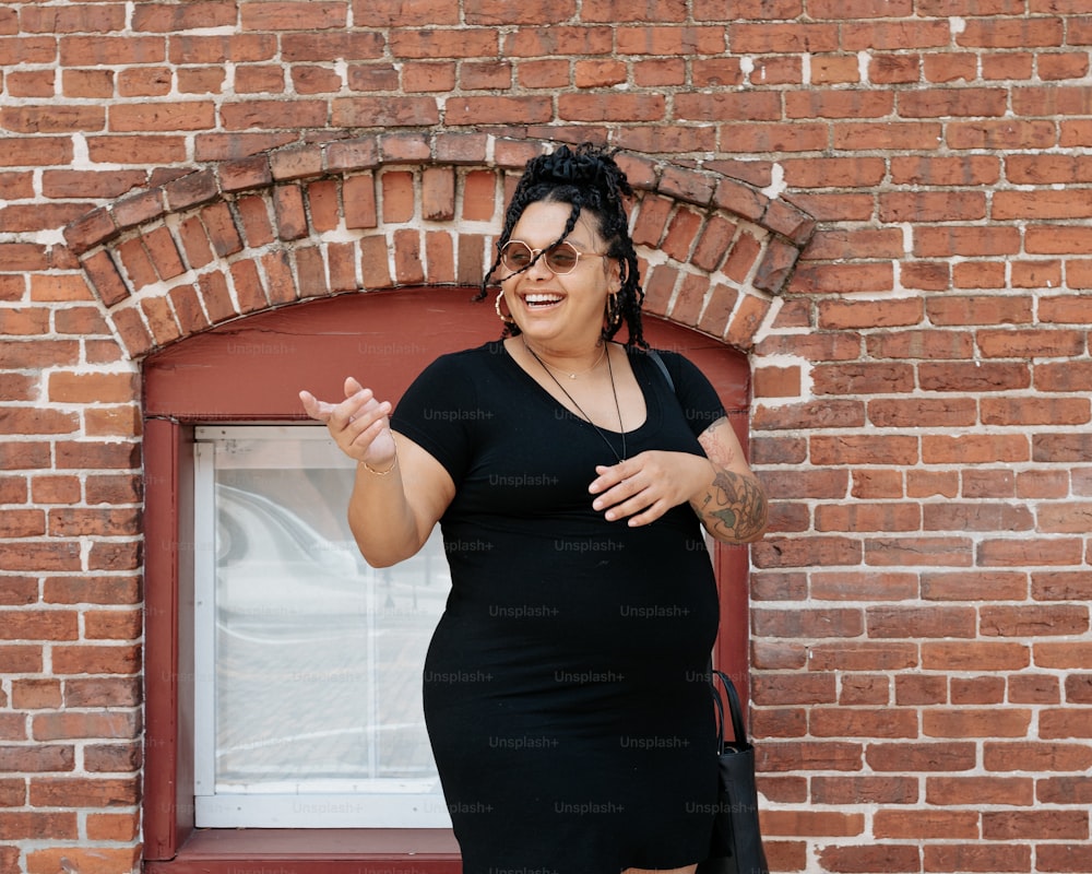 Eine Frau in einem schwarzen Kleid steht vor einer Ziegelmauer