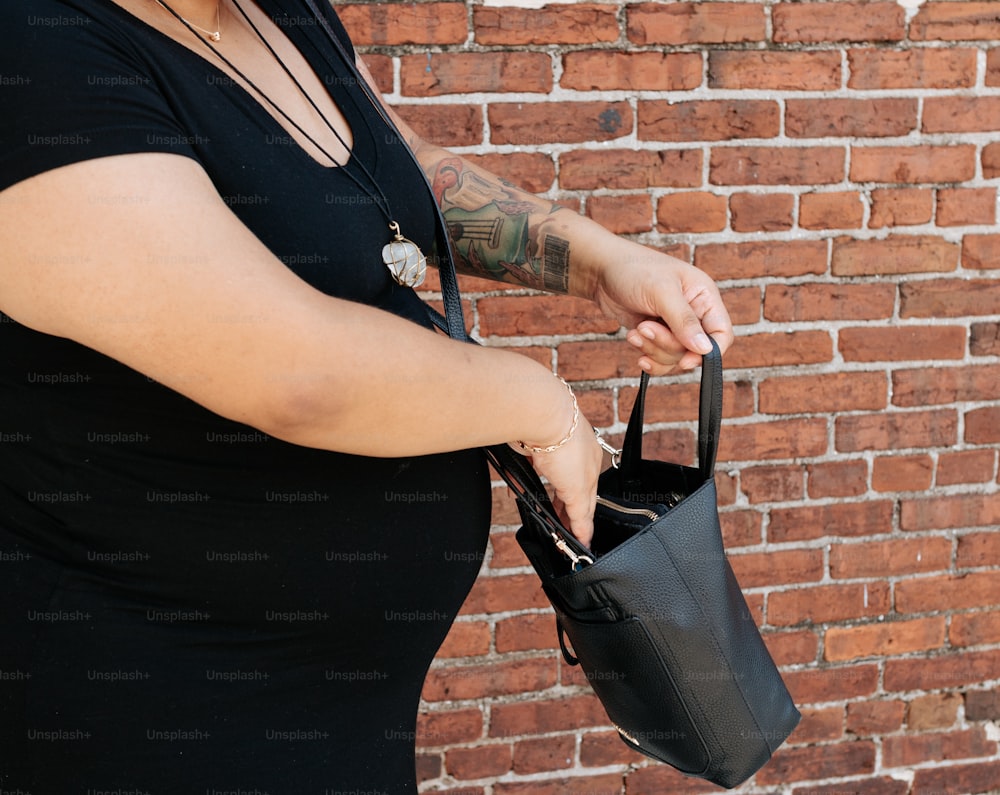 レンガの壁の前で黒い財布を持つ女性