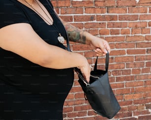 a woman holding a black purse in front of a brick wall