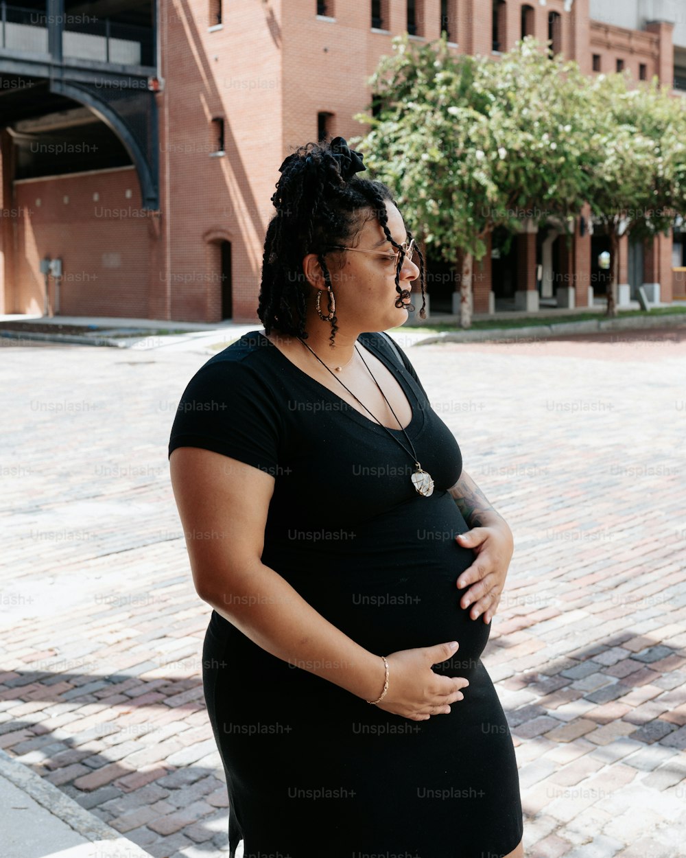 Une femme enceinte en robe noire debout devant un bâtiment en briques