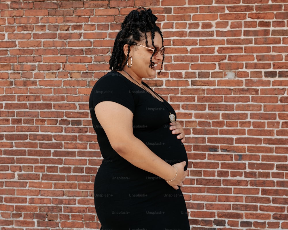 a pregnant woman standing in front of a brick wall