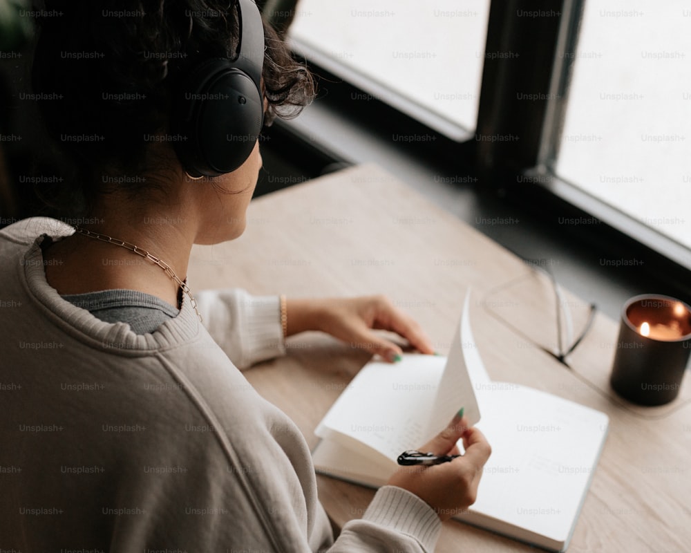 a woman sitting at a table with a book and headphones