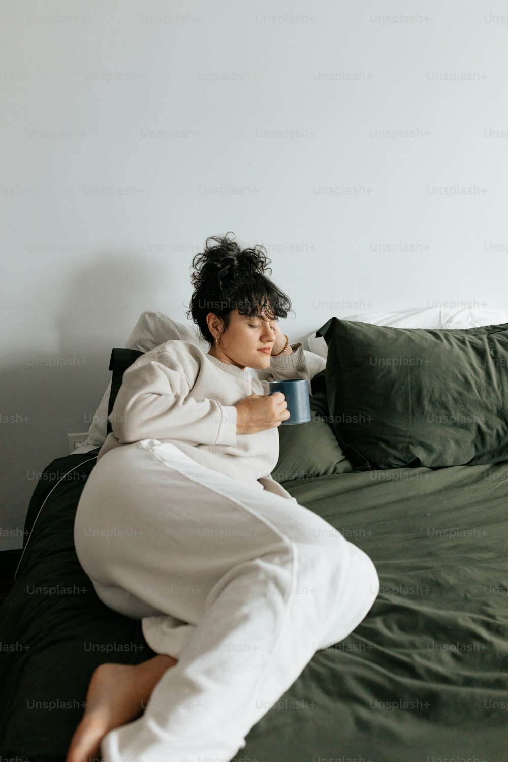 a woman laying on top of a bed holding a cup