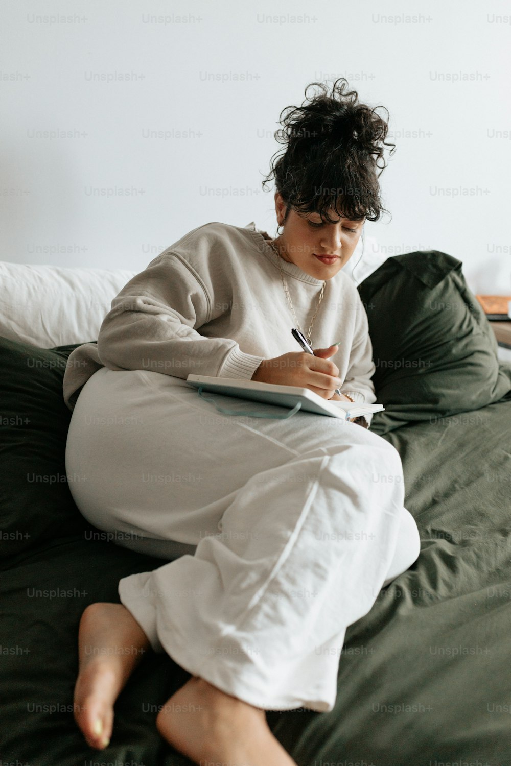 a woman sitting on a bed writing on a notepad