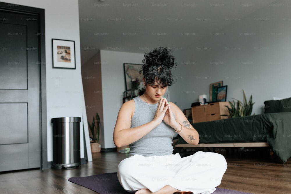 uma mulher sentada em um tapete de ioga em um quarto