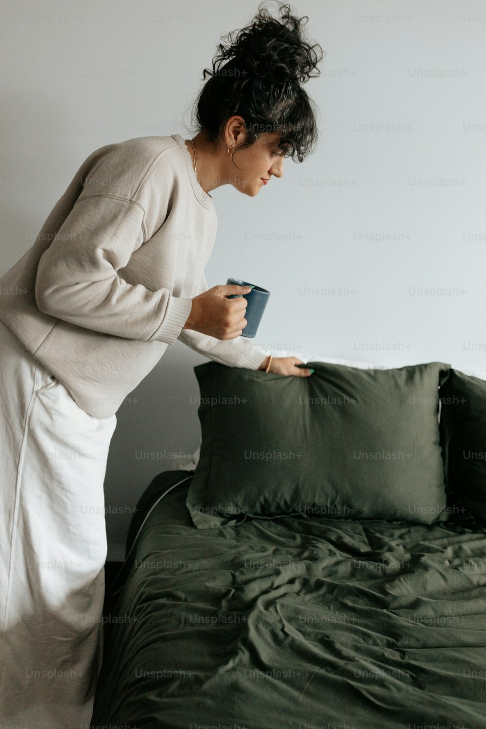 a woman standing over a bed holding a cup of coffee
