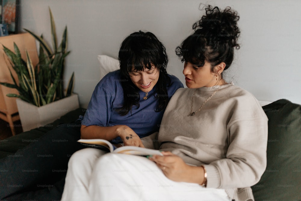 two women sitting on a couch looking at a book