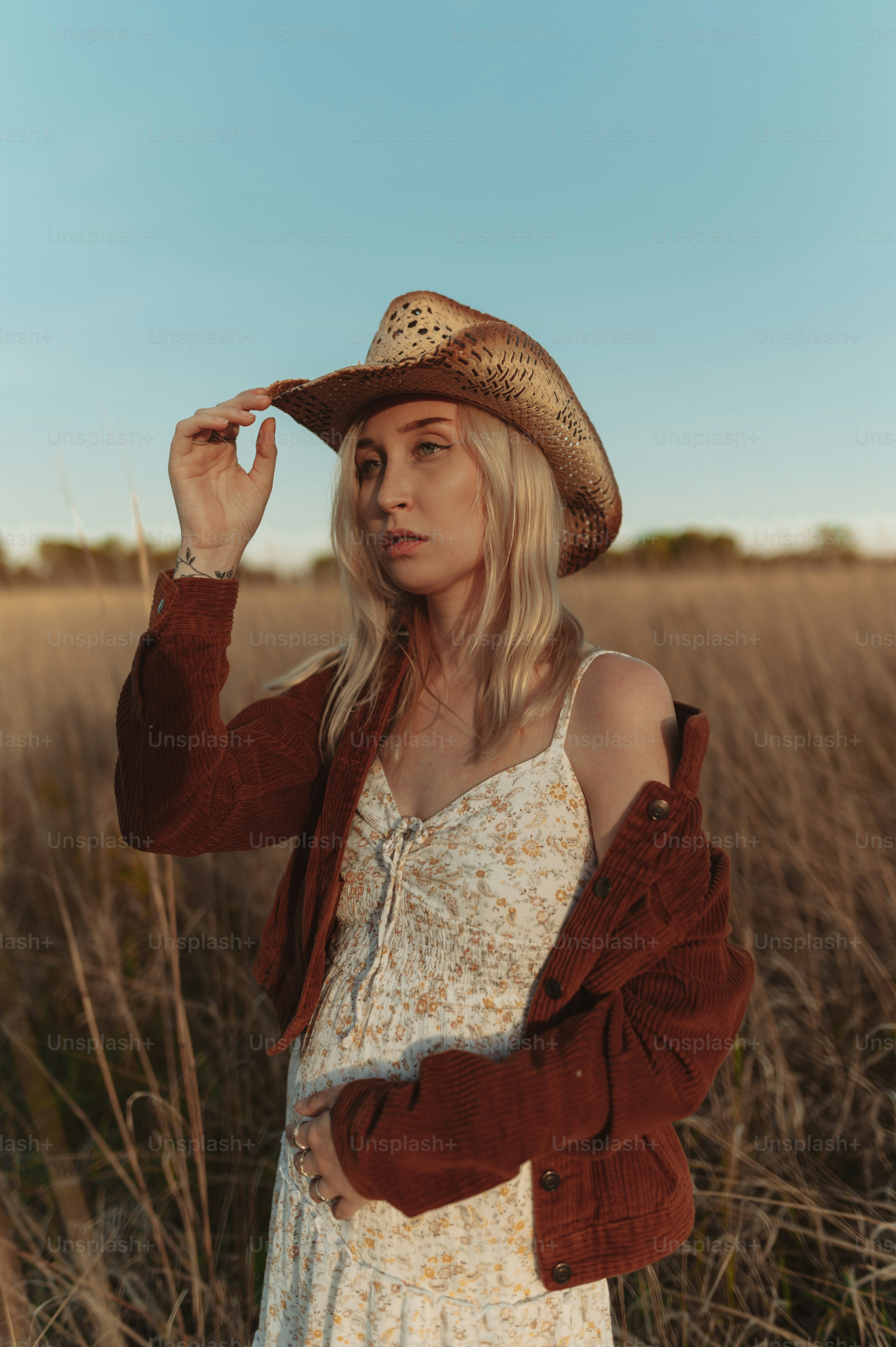 a woman standing in a field wearing a hat