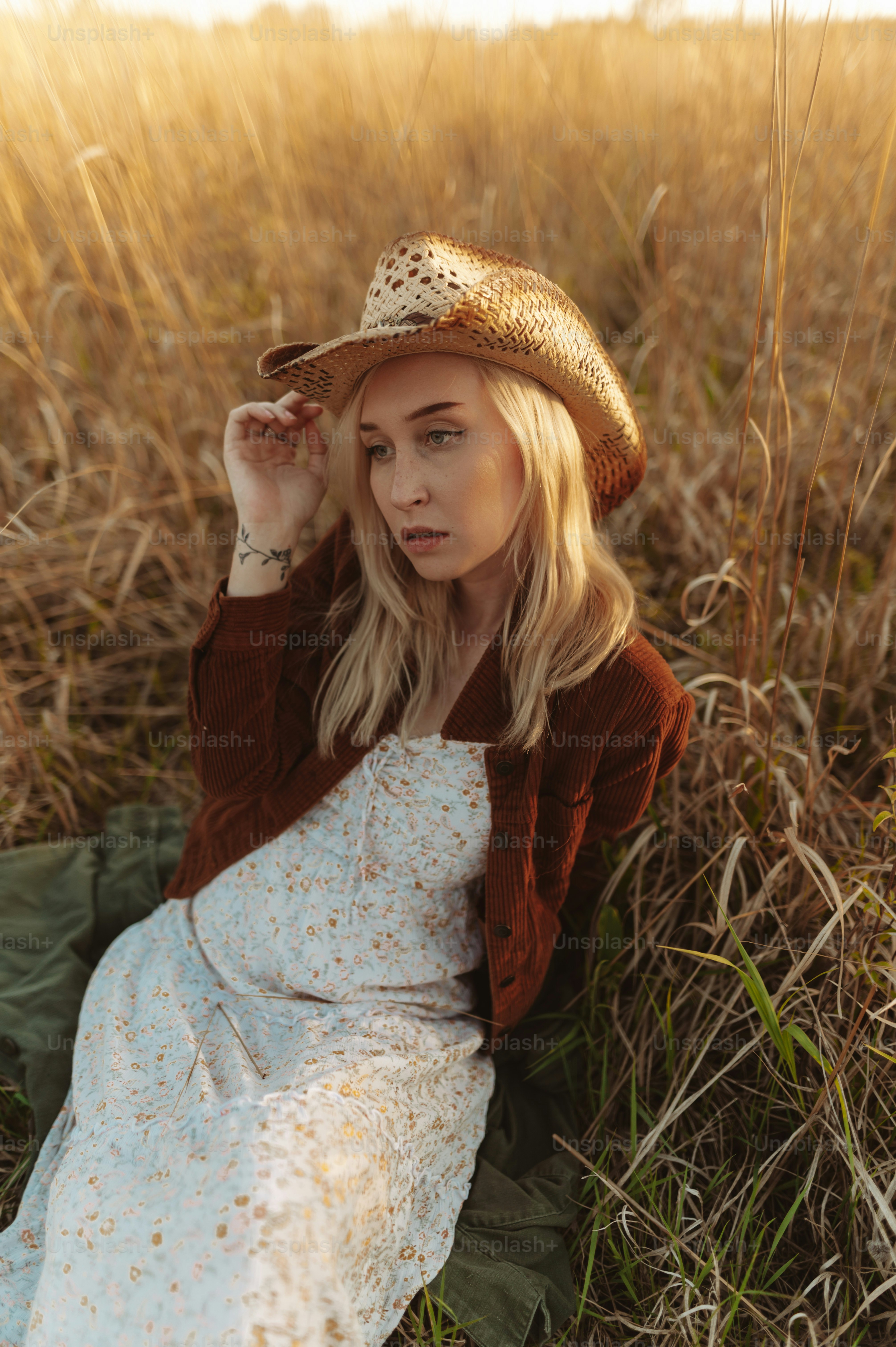 a woman sitting in a field wearing a hat