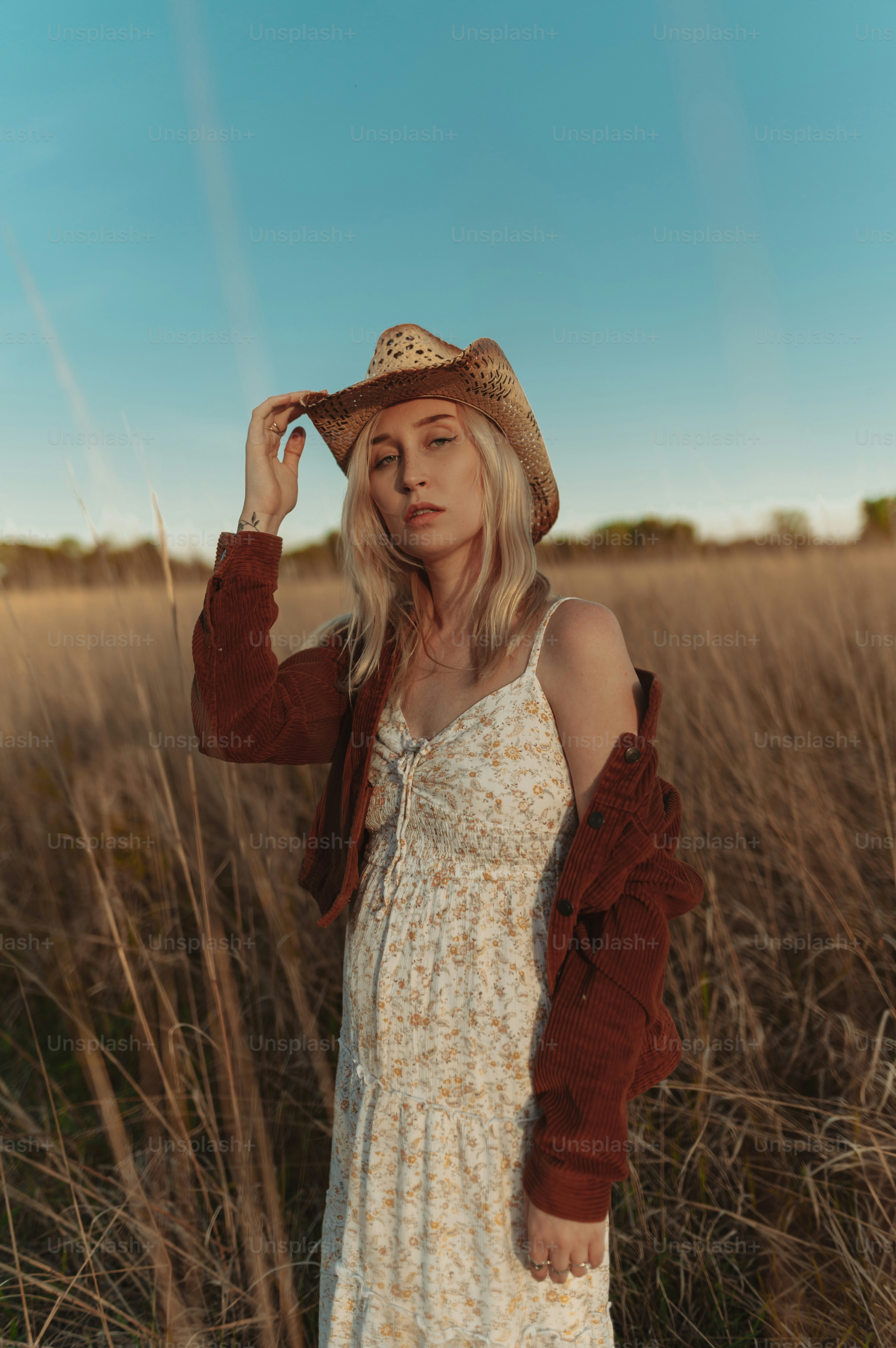 a woman standing in a field wearing a hat