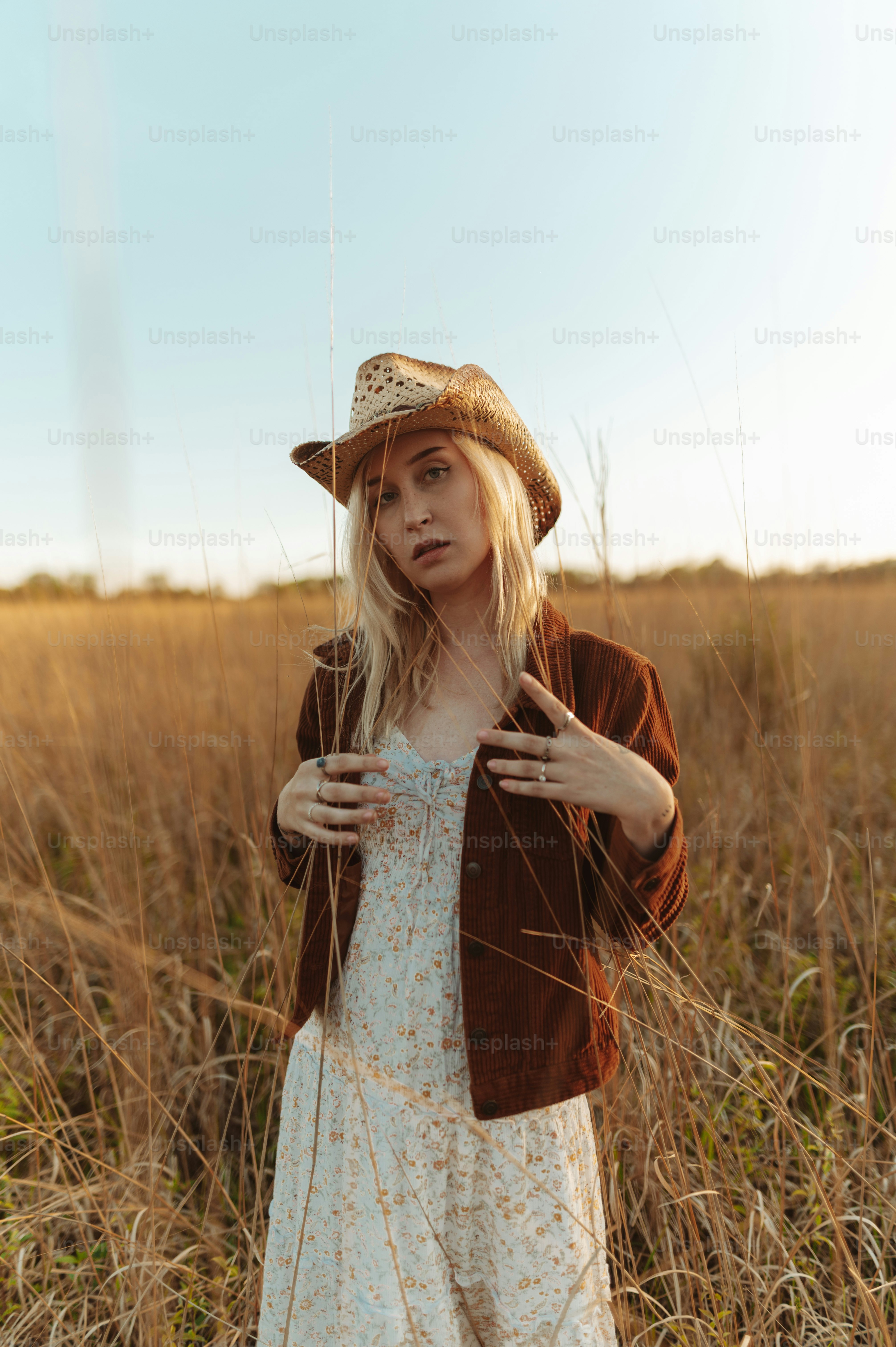 a woman standing in a field wearing a hat