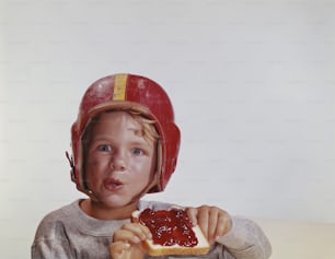 a young boy wearing a helmet eating a sandwich