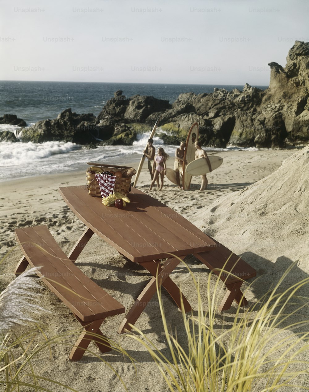 a wooden picnic table on a beach with people in the background