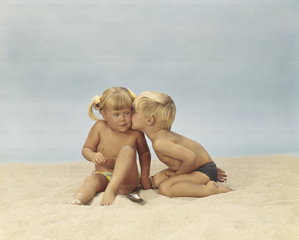 a couple of kids sitting on top of a sandy beach
