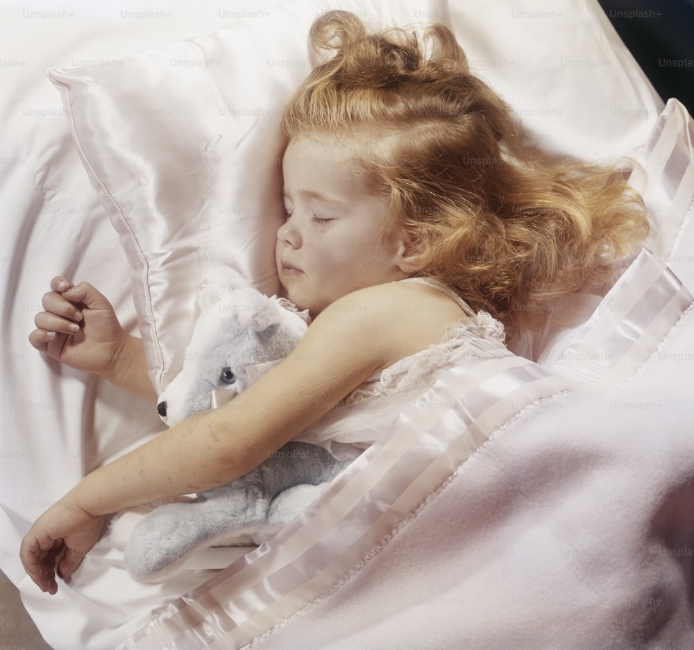 a little girl laying in a bed with a teddy bear