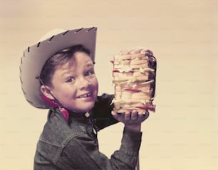 um garoto usando um chapéu de cowboy segurando um sanduíche
