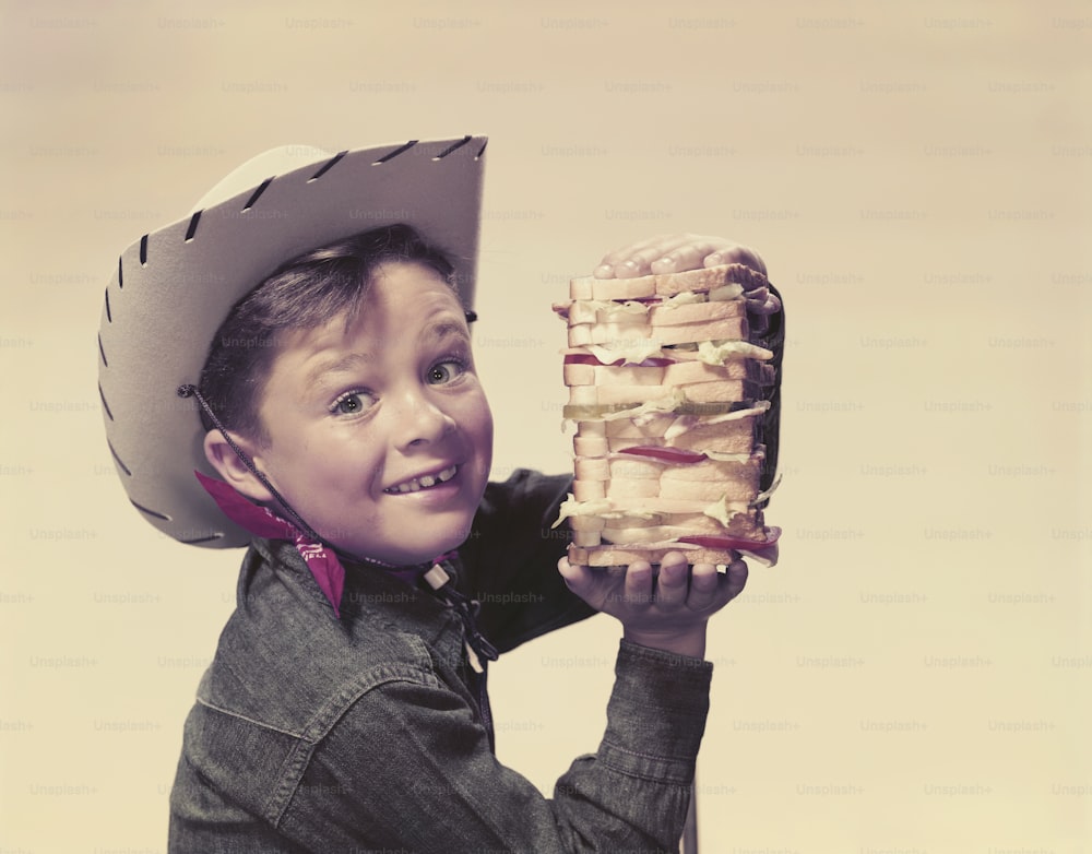 a young boy wearing a cowboy hat holding a sandwich