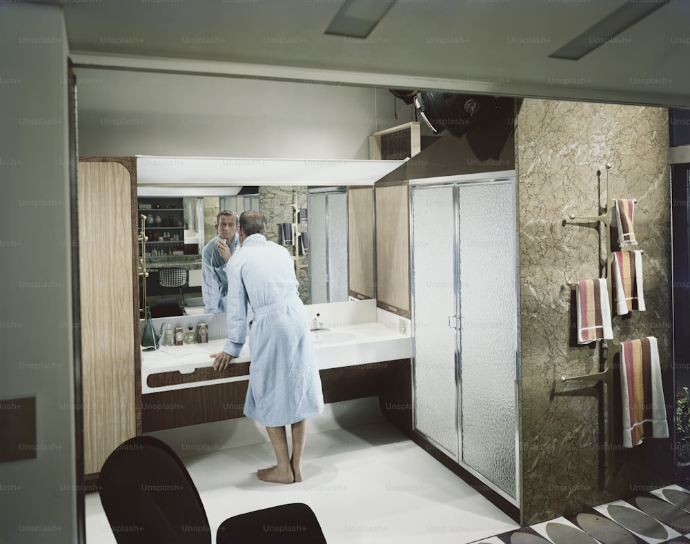 a man in a bathrobe standing in front of a sink