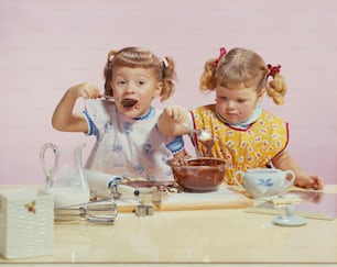 Zwei kleine Mädchen, die an einem Tisch sitzen und Schokolade essen