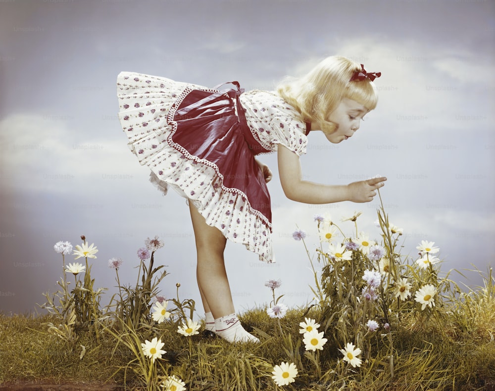 a little girl in a dress reaching for daisies
