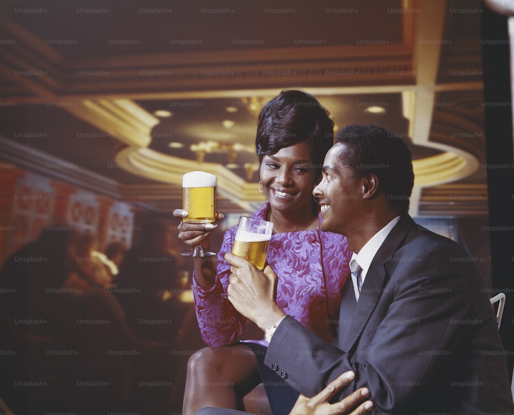 a man and a woman sitting next to each other holding a glass of beer