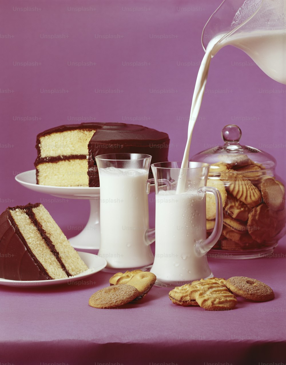 a table topped with cakes and cookies next to a glass of milk