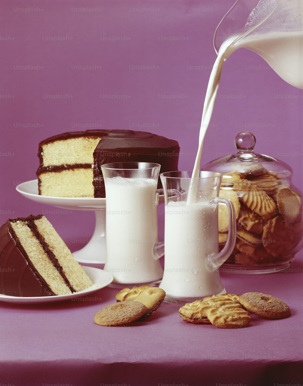a table topped with cakes and cookies next to a glass of milk