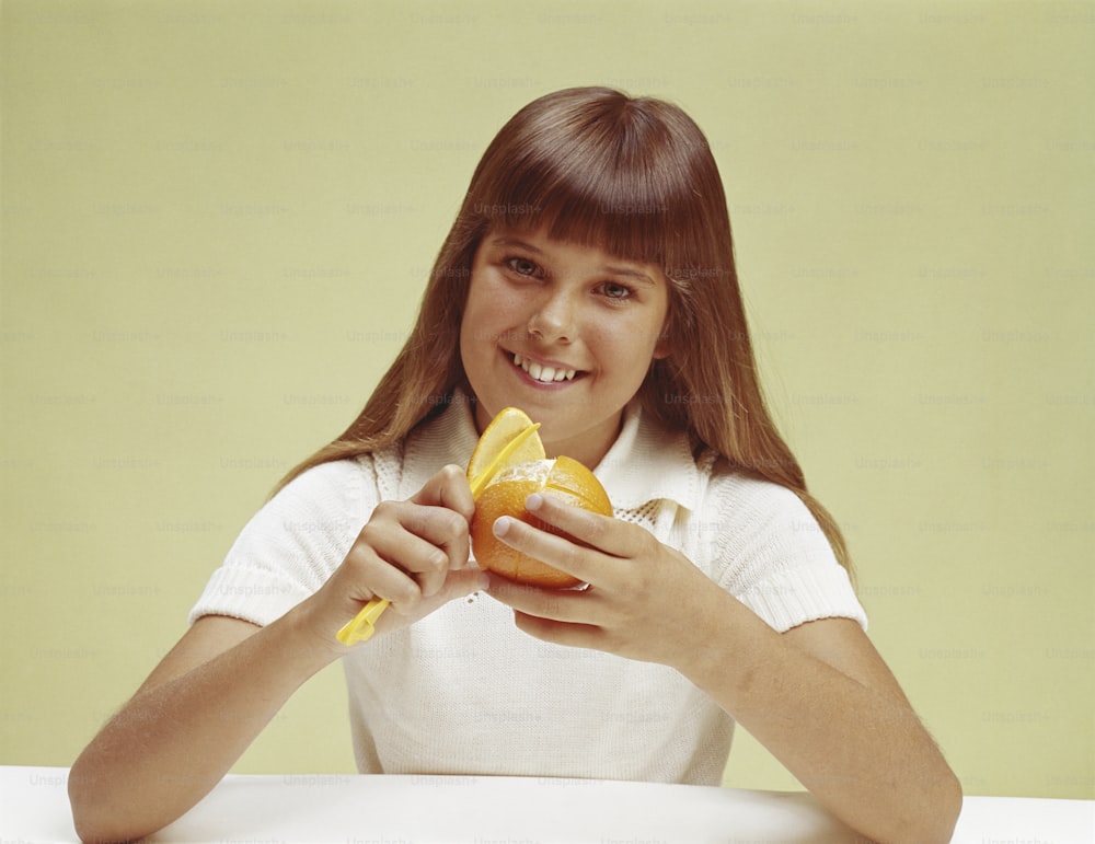 若い女の子が皮をむいたオレンジを持っている