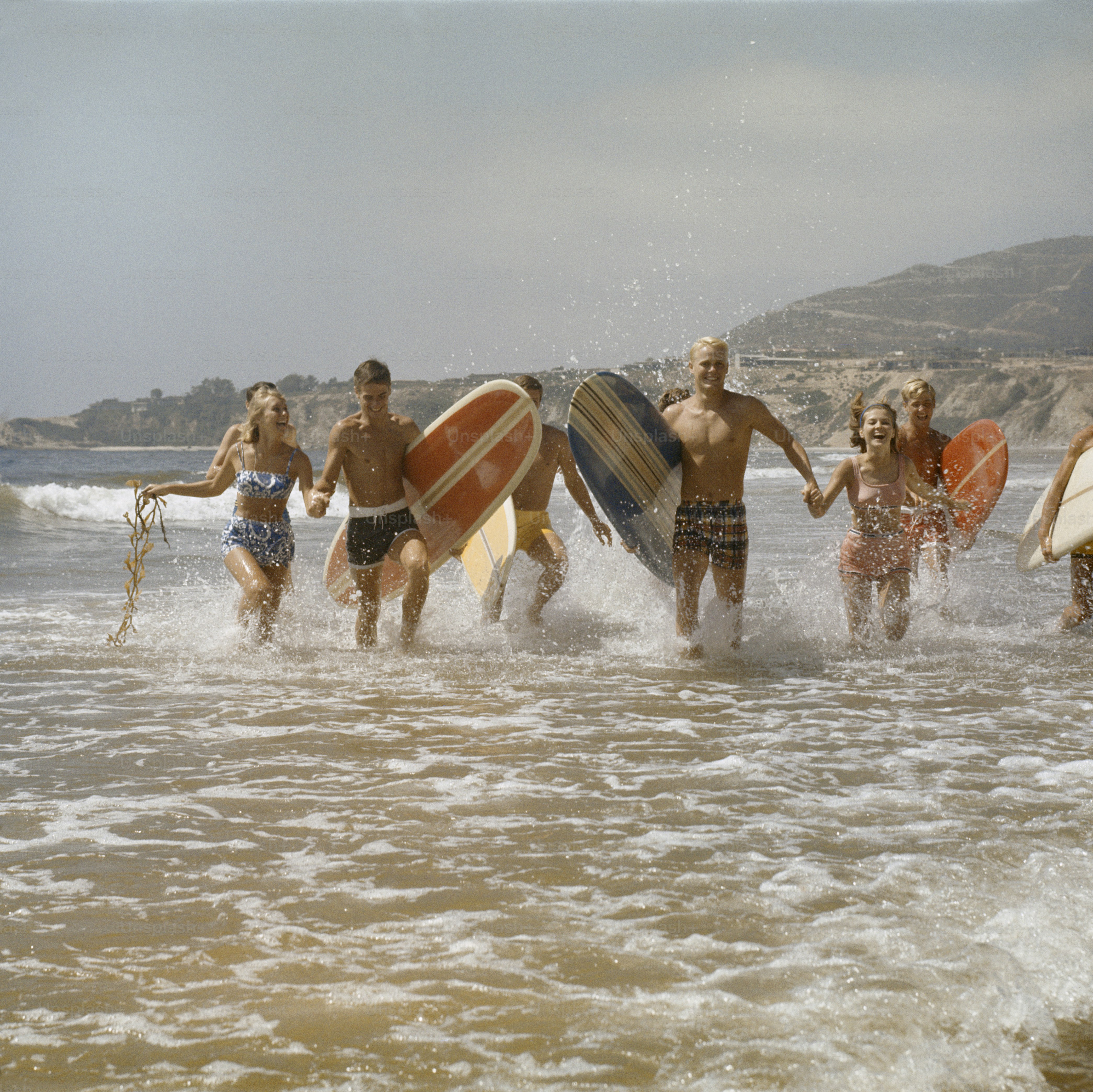 a group of people running into the ocean with surfboards