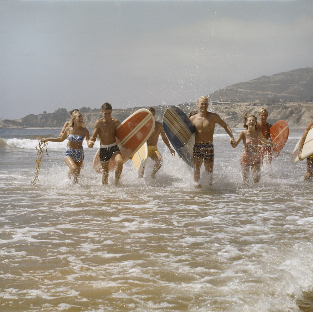 a group of people running into the ocean with surfboards