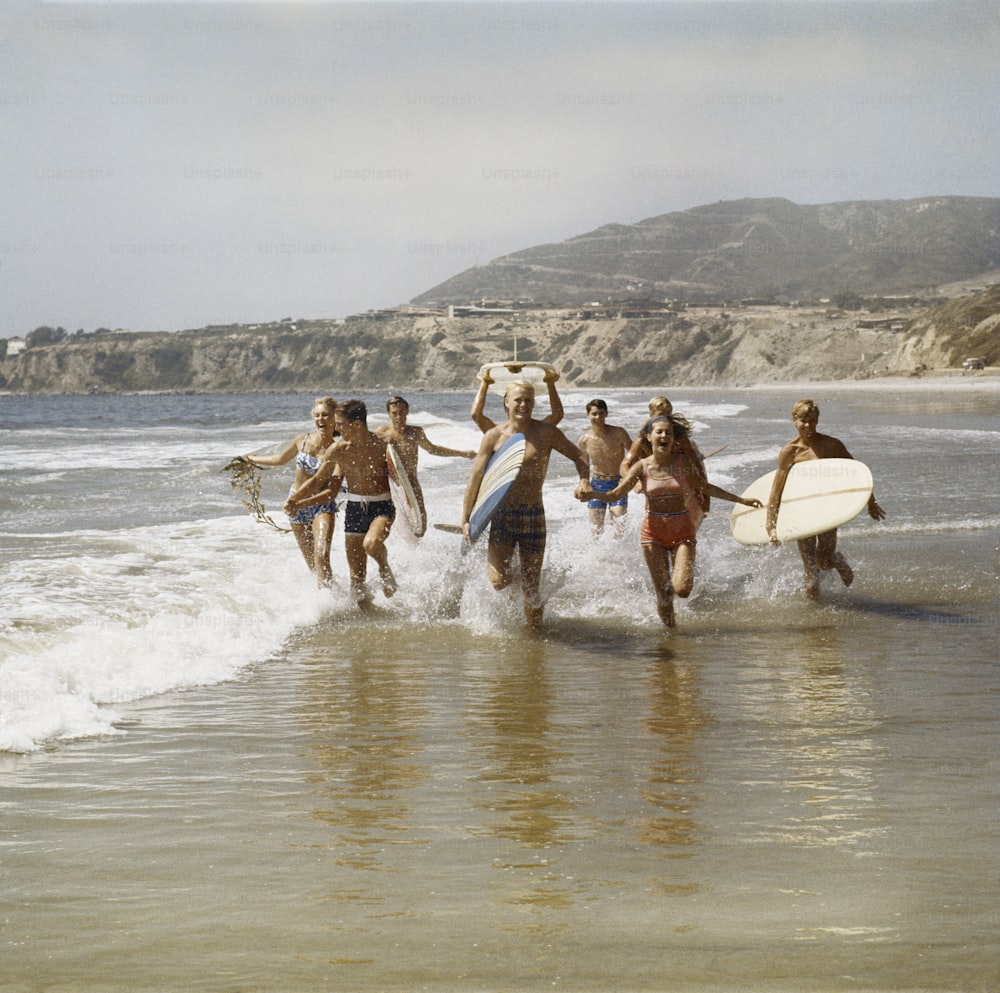 a group of people running into the ocean with surfboards