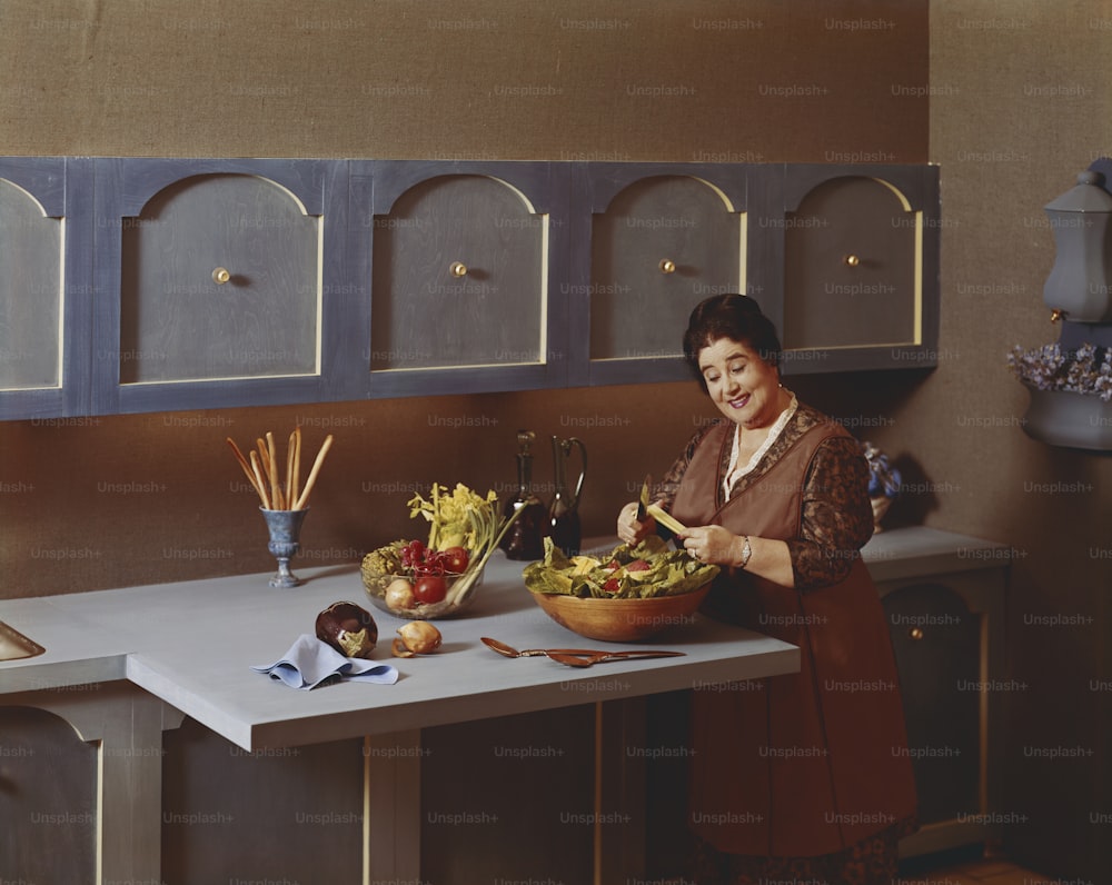 a woman standing at a kitchen counter preparing a salad