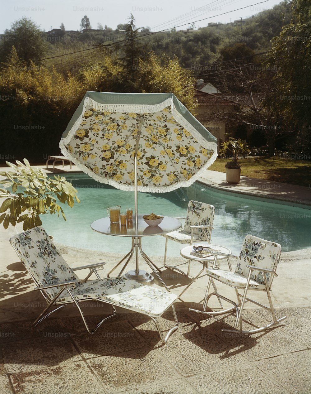 une table avec des chaises et un parasol à côté d’une piscine