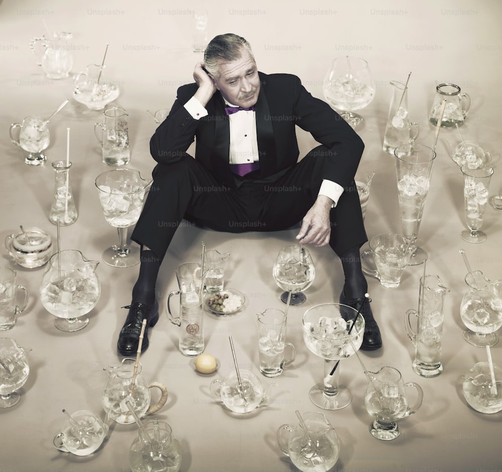 a man in a tuxedo sitting in front of a table full of glass