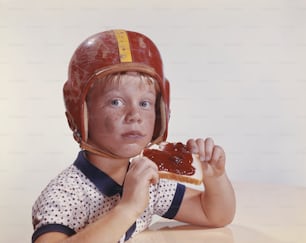 a young boy wearing a helmet and holding a sandwich