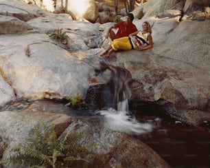 a man and a woman sitting on a rock next to a waterfall