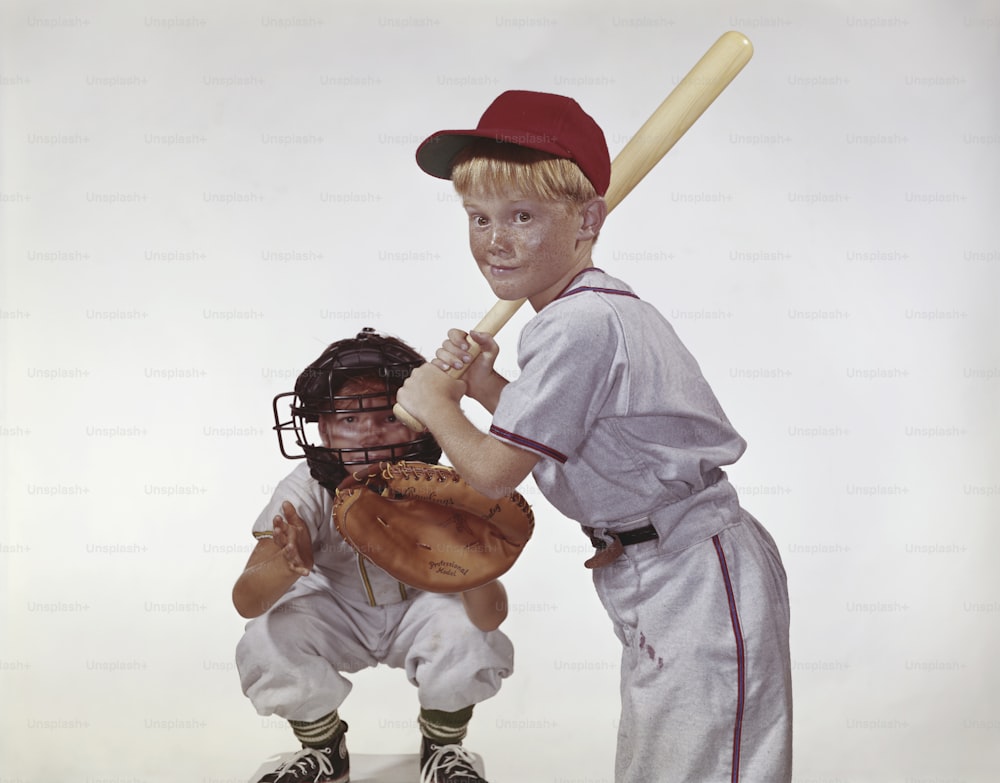 Ein kleiner Junge, der einen Baseballschläger neben einem kleinen Jungen in einer Baseballuniform hält