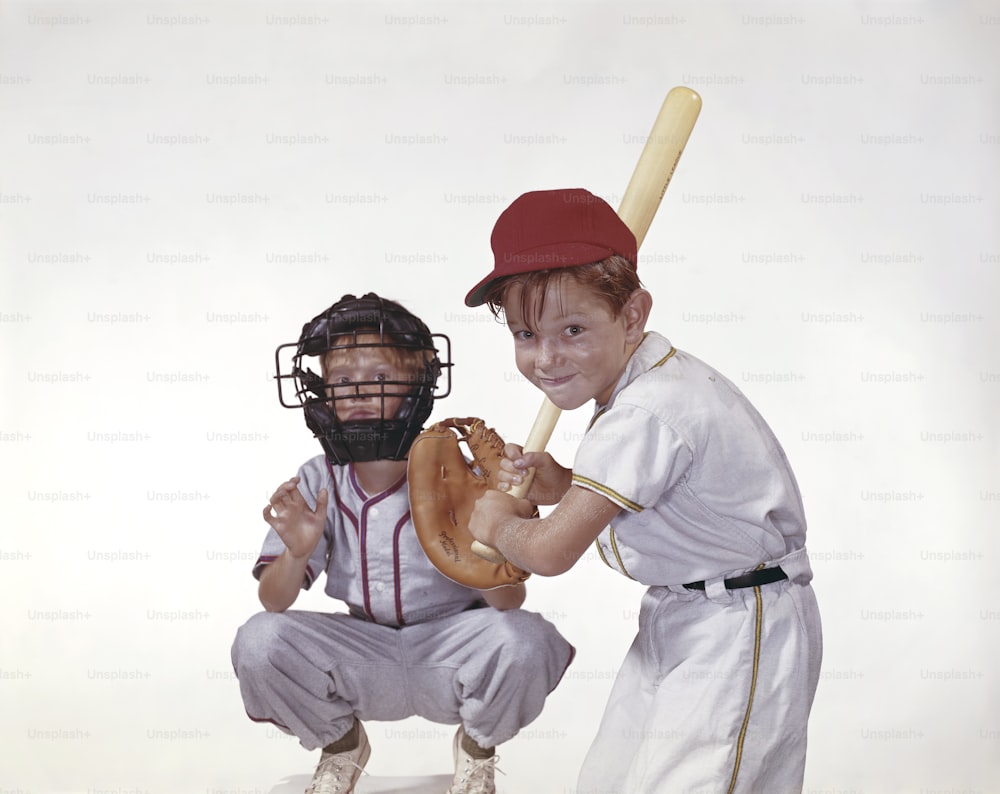 a young boy holding a baseball bat next to a young boy in a baseball uniform