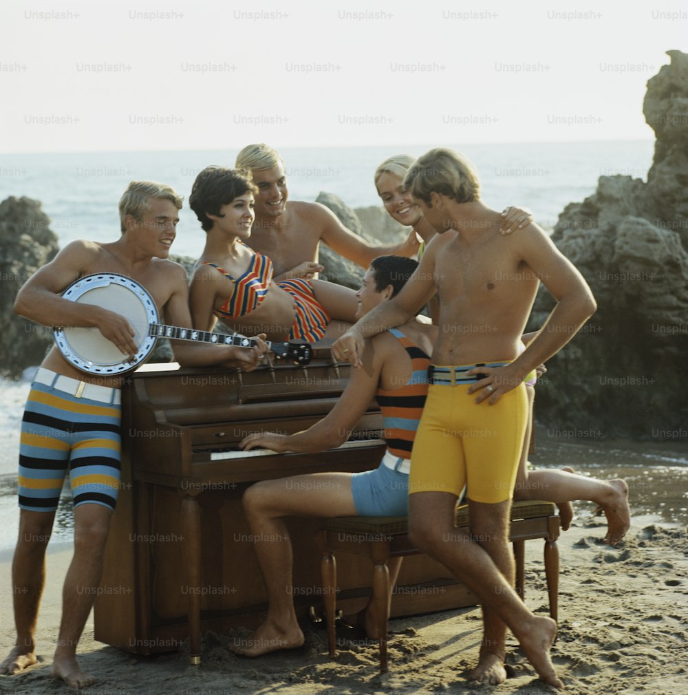 a group of men standing around a piano on a beach