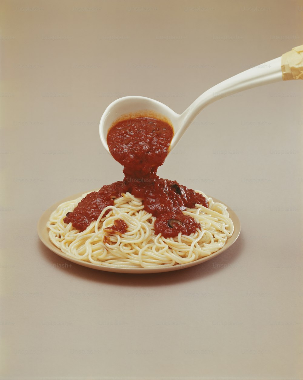 ein Löffel, der Sauce auf einen Teller Spaghetti gießt