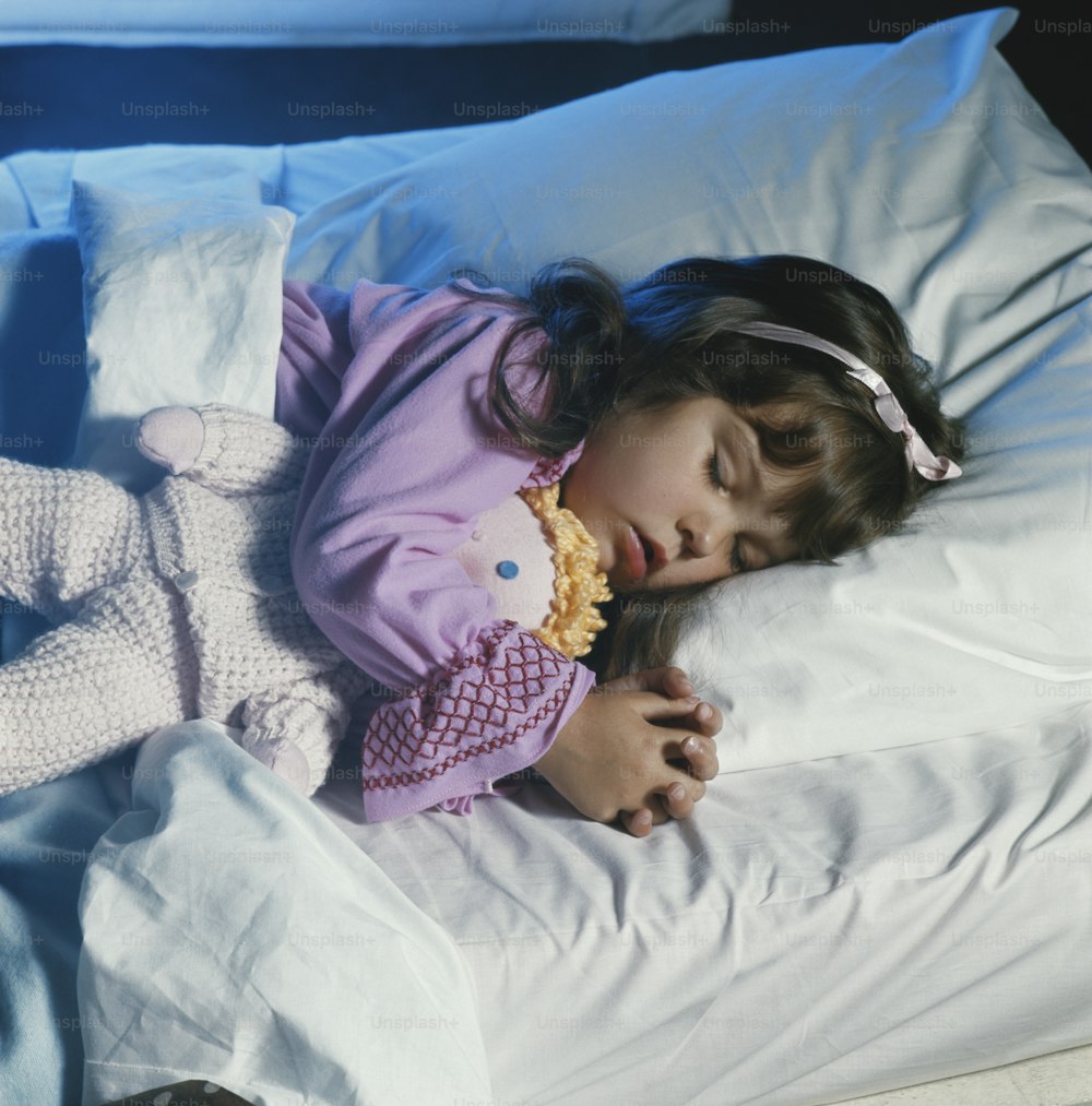 a little girl sleeping on a bed with a stuffed animal