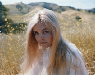 a woman with long blonde hair sitting in a field