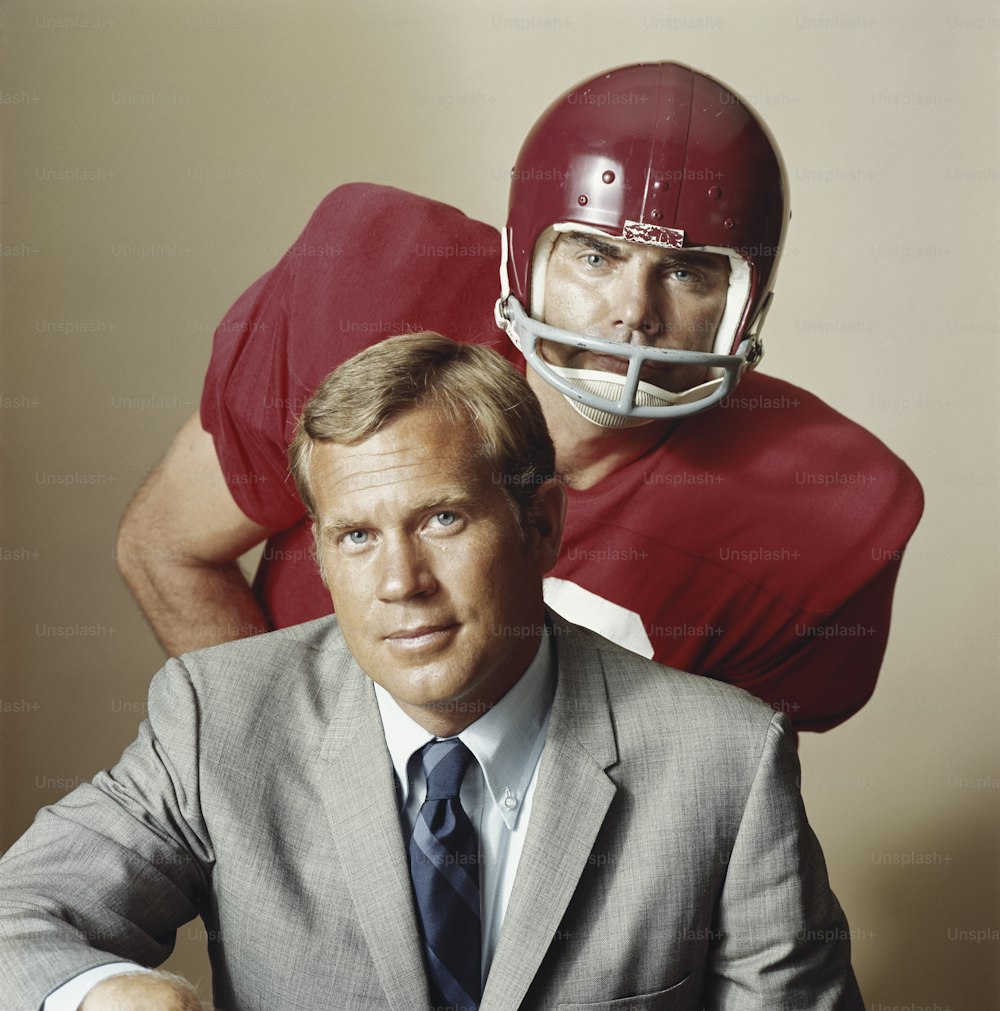 a man in a suit and tie sitting next to a football player