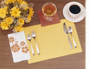 uma mesa com um tapete amarelo, talheres e uma xícara de café