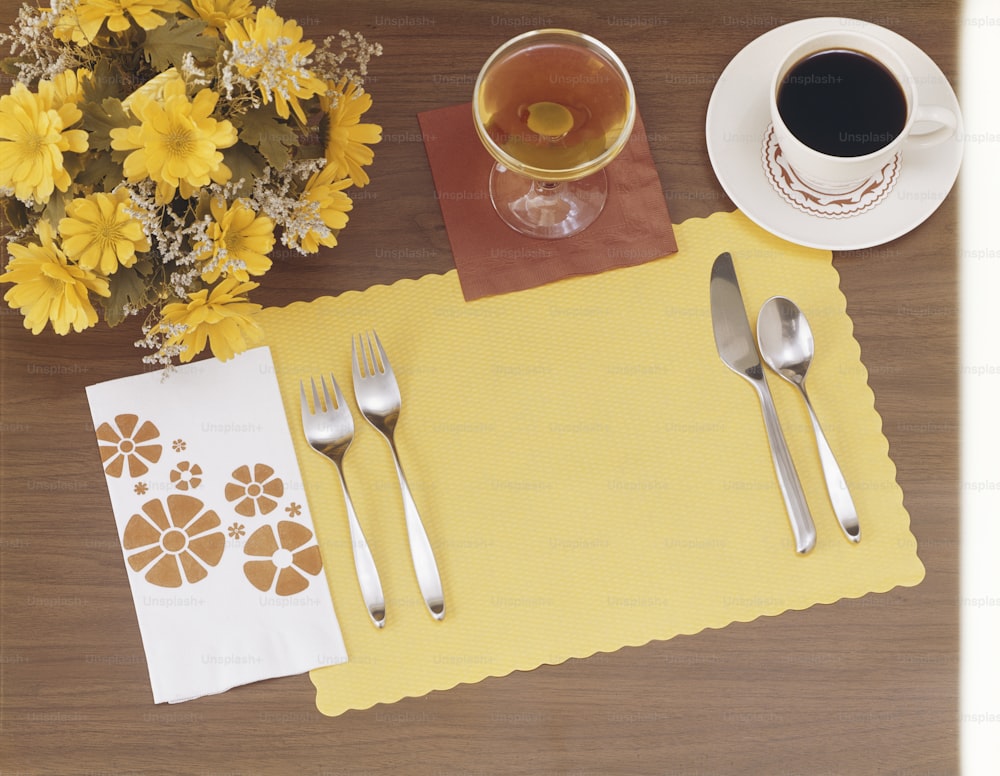 a table with a yellow place mat, silverware and a cup of coffee