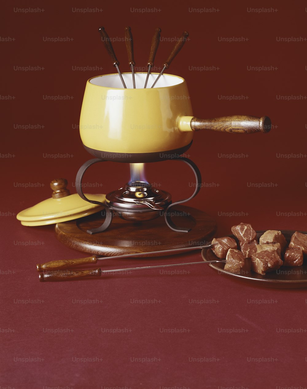 a yellow fonding pot with a wooden spoon and a plate of brown sugar cube