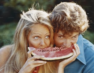 a man and a woman eating a slice of watermelon