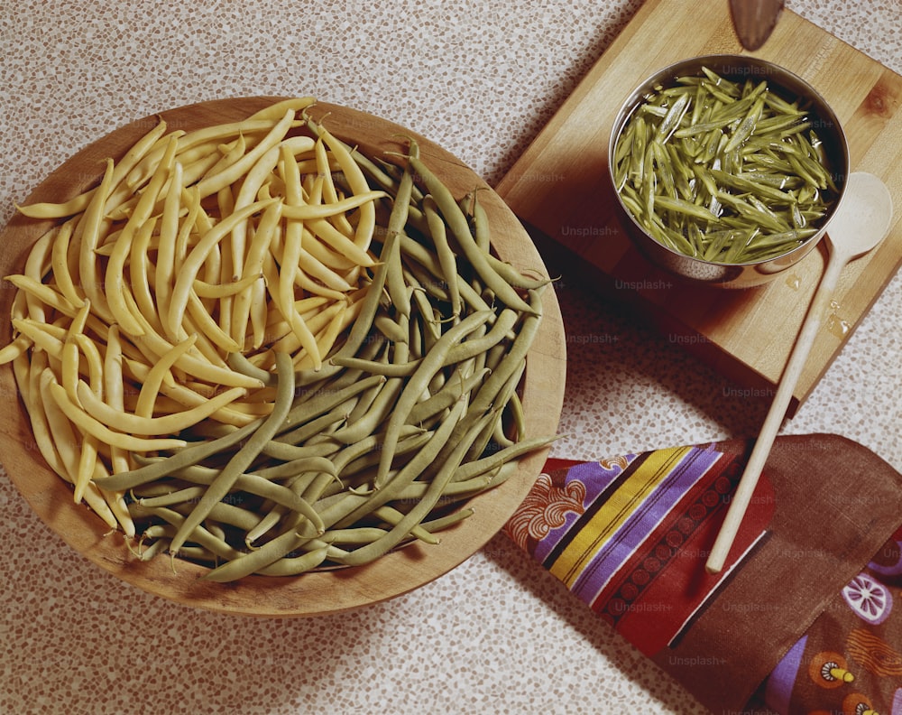 a wooden bowl filled with green beans next to a bowl of brown beans